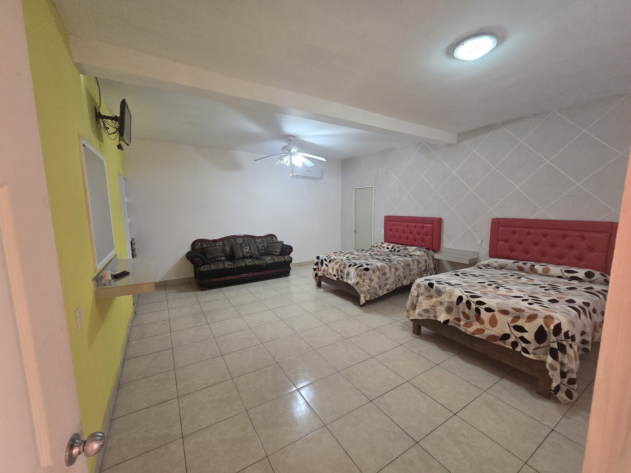 Habitación amplia de Hostal El Primo con dos camas matrimoniales y sofá grande